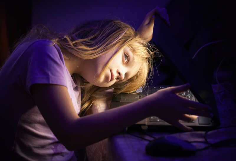 小女孩侧着头玩笔记本电脑