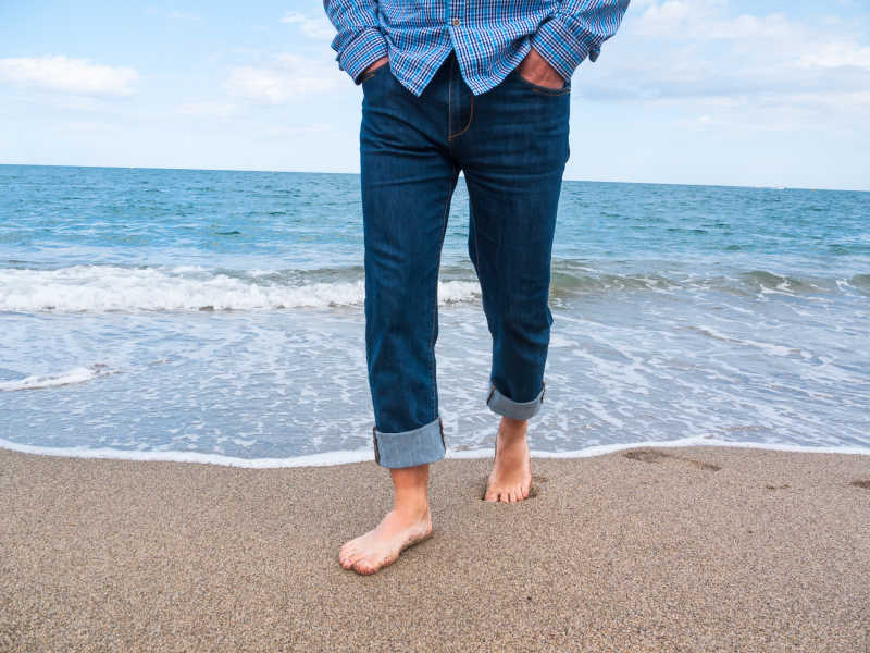 穿着牛仔裤赤脚走在海边的男人