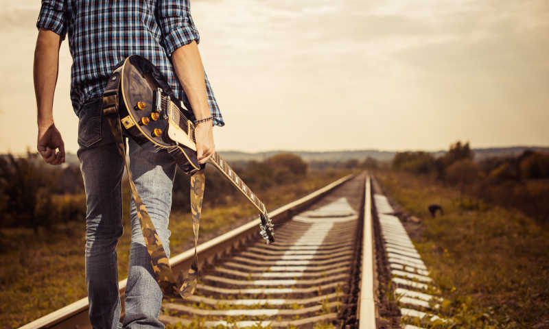 拿着吉他走在铁路上的男人