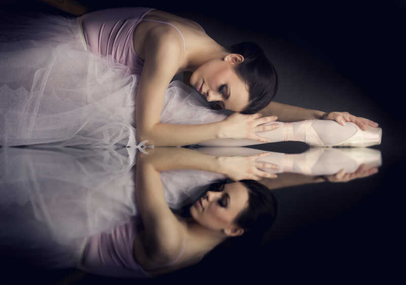 躺在镜子上练习的芭蕾舞者有着倒影