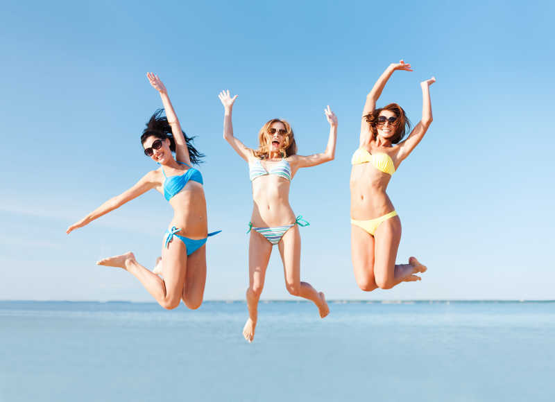 夏日海滩上跳跃的三个年轻性感女子