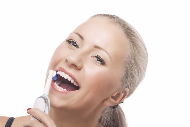 金发白人妇女用电动牙刷刷牙