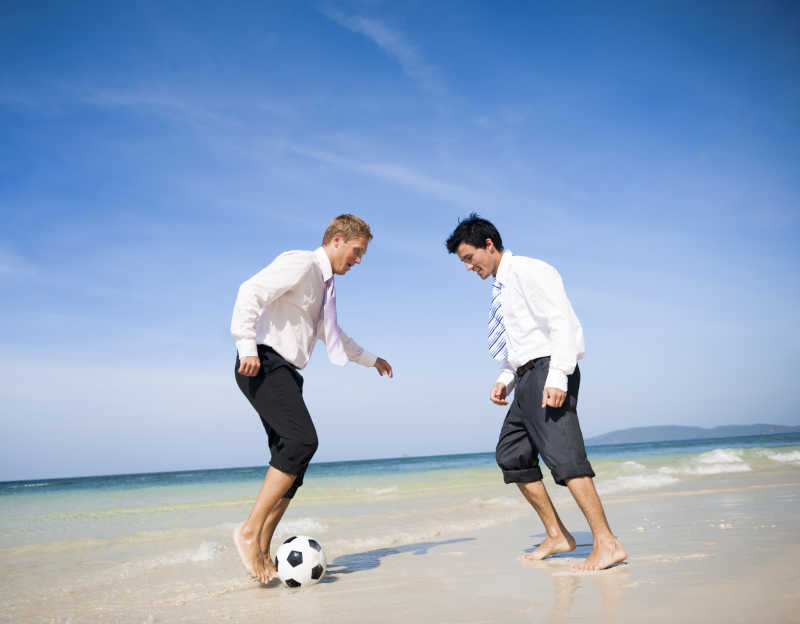 海滩上的两个商人在踢足球