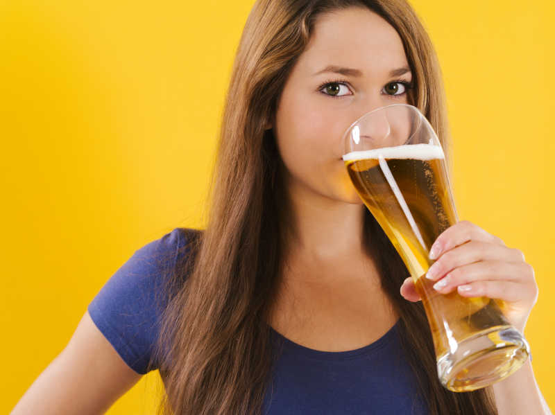黄色背景下喝啤酒的女人