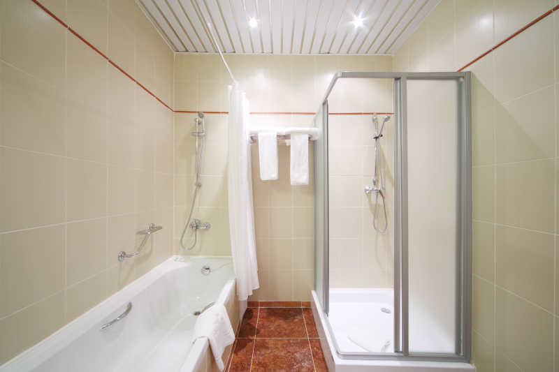 浅色的浴室内的白色浴缸和玻璃围挡冲凉房