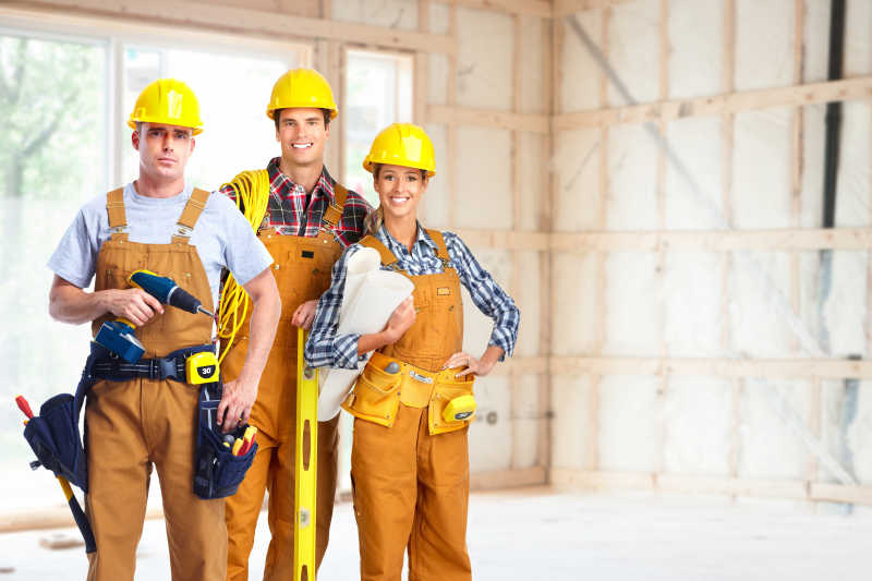 未完成装修的室内背景下三个戴着黄色安全帽拿着工具的工人