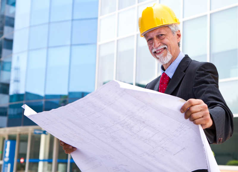 戴着黄色安全帽的建筑师站在大楼前看图纸