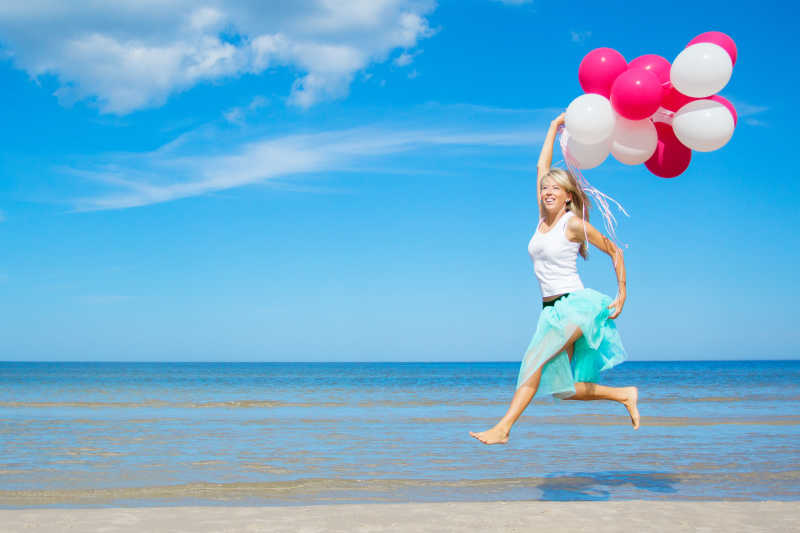 海边拿着气球快乐跳跃的美女