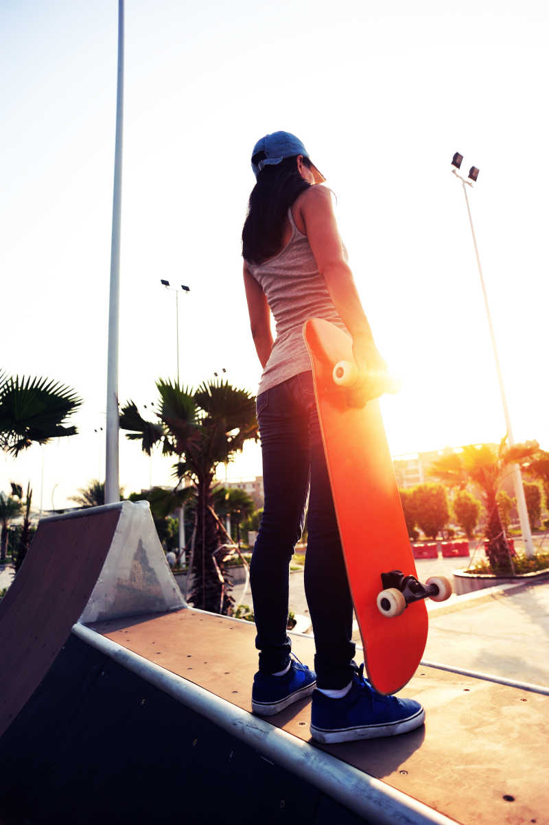夕阳下拿着滑板站在长廊上的年轻女子