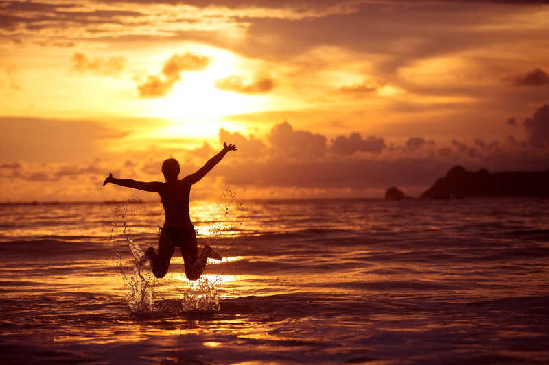 落日时分在海中跳跃的女孩剪影