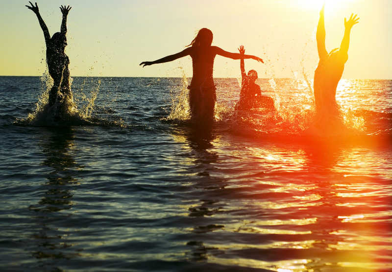 日落时分在海洋中跳跃的年轻朋友剪影