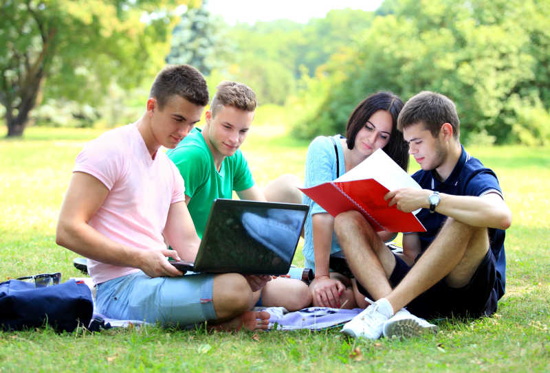 绿色公园里学习的大学生拿着红色课本和笔记本电脑
