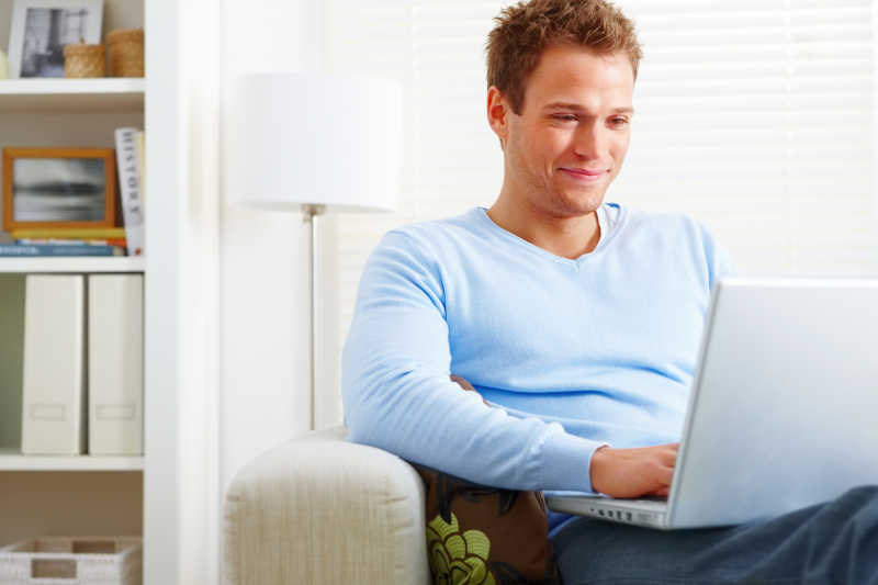 微笑的中年男人坐在家里的沙发上使用笔记本电脑