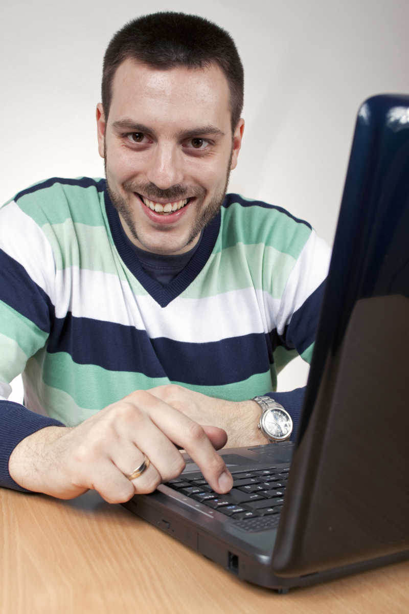 面带笑容的男子坐在沙发上使用笔记本电脑