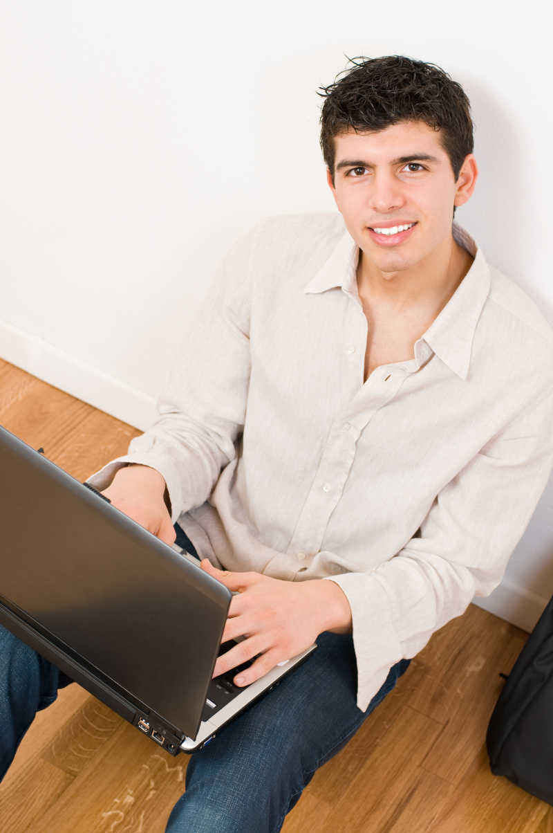 穿着休闲服的快乐的年轻人在使用他的笔记本电脑