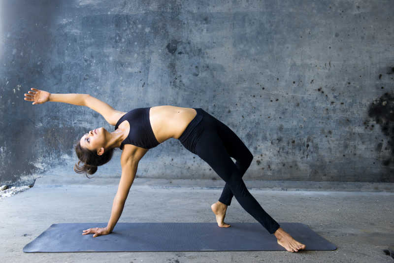 灰色水泥墙背景下练习高级瑜伽的女子