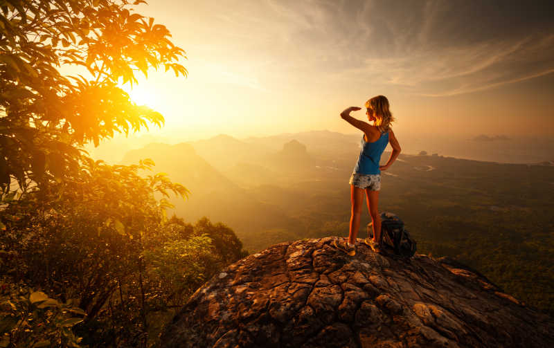 站在岩石上看日出的美女旅行者