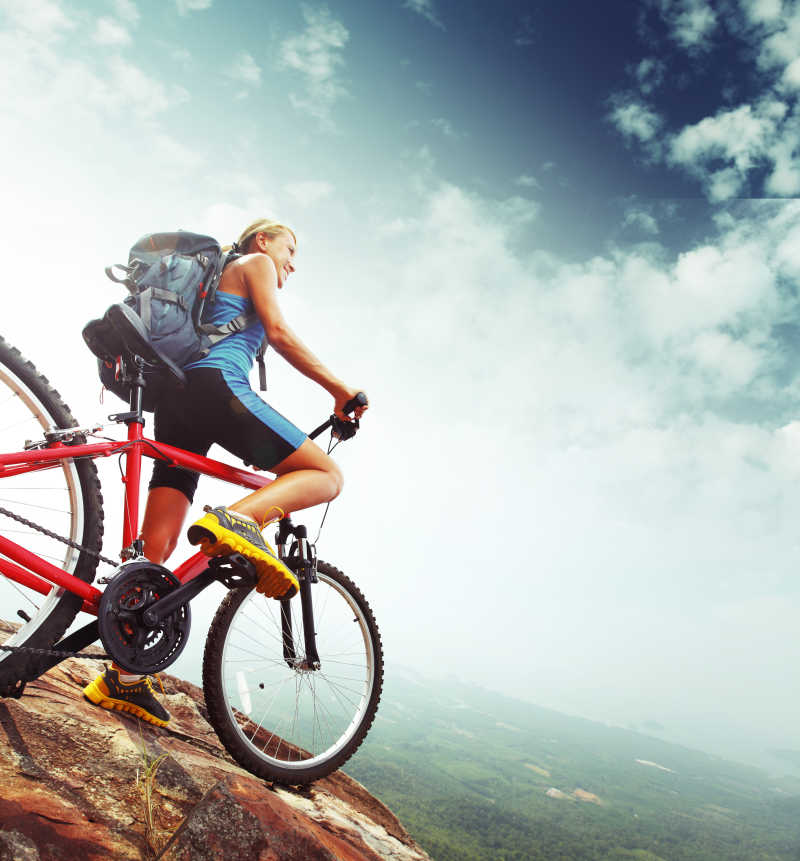 骑着自行车背着背包在岩石上看风景的美女