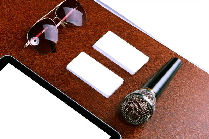 木色桌面上的白色空白纸话筒和太阳镜
