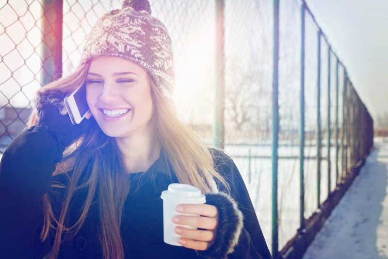 冬季走在户外拿着咖啡打电话的女人