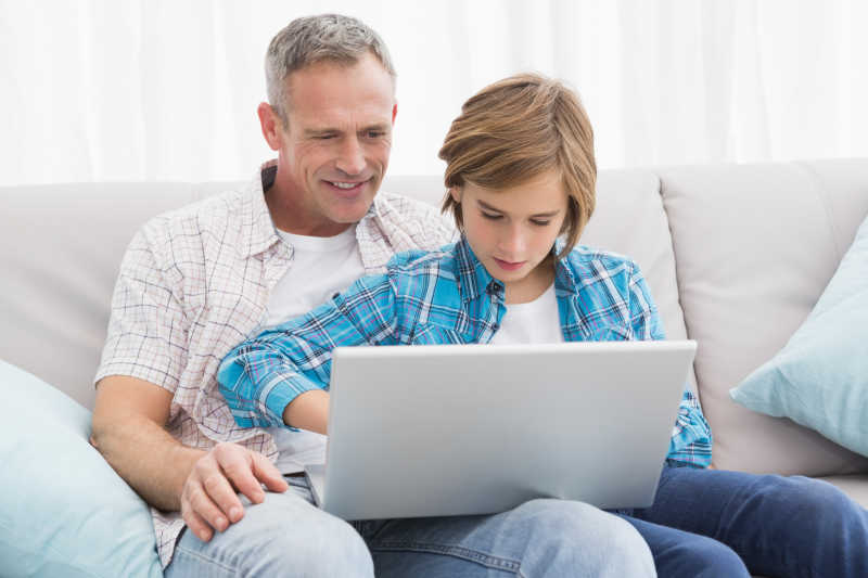 父亲与儿子坐在沙发上使用笔记本电脑