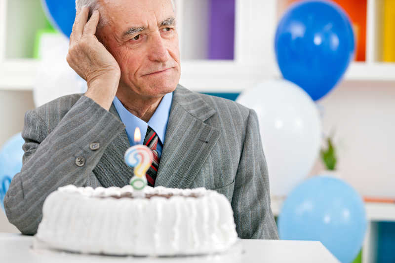 老人坐在生日蛋糕前努力回忆起年龄是多少岁
