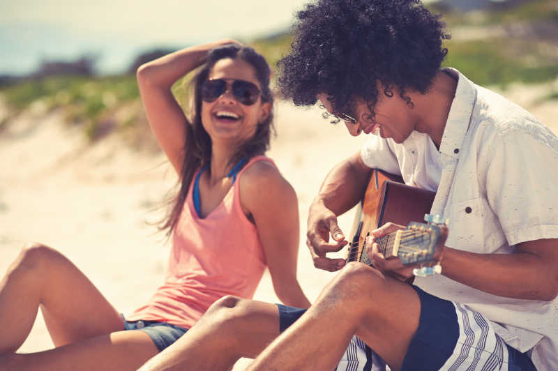 可爱的西班牙裔夫妇弹吉他为海滩上的爱和拥抱