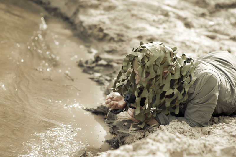 一个军事伪装的人在河边喝水