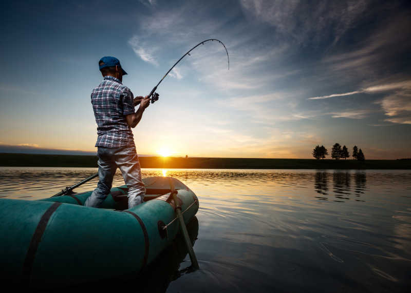 成熟的男人在日落时在池塘钓鱼