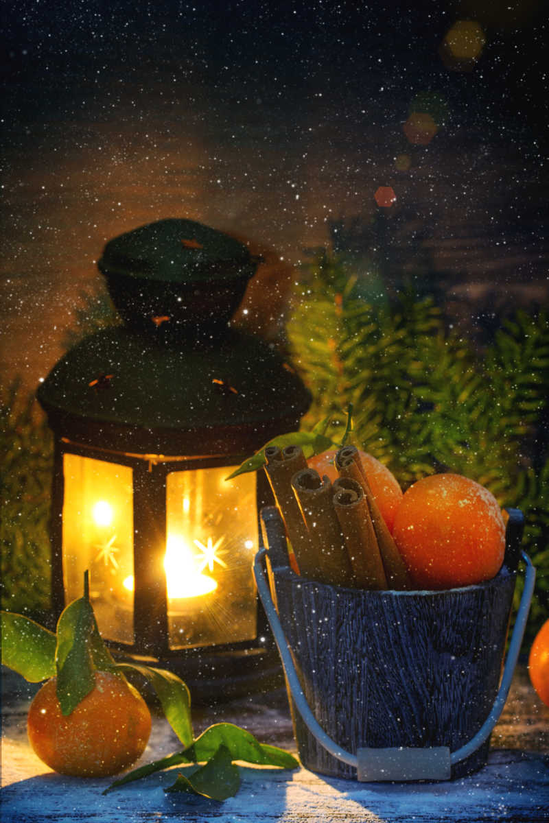 在圣诞树背景下燃烧的灯笼橘子和肉桂木桶