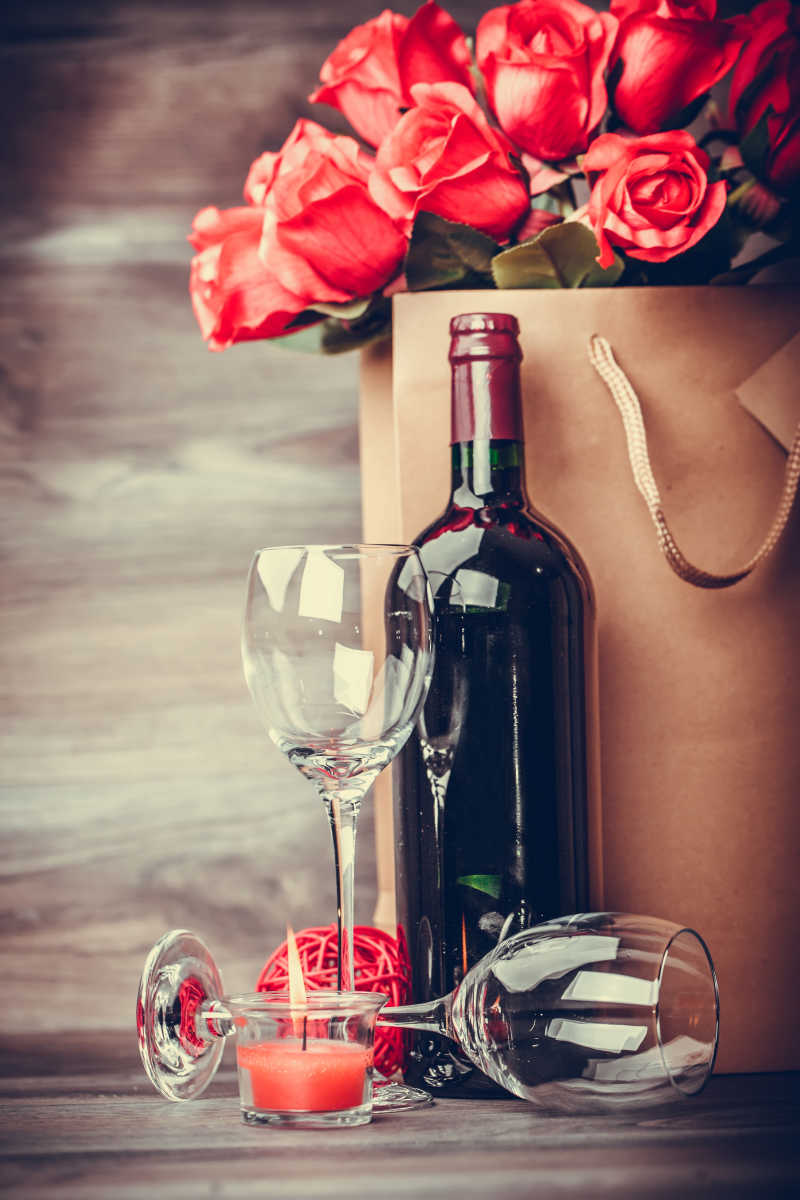 红酒和玫瑰放在木桌上的纸袋里