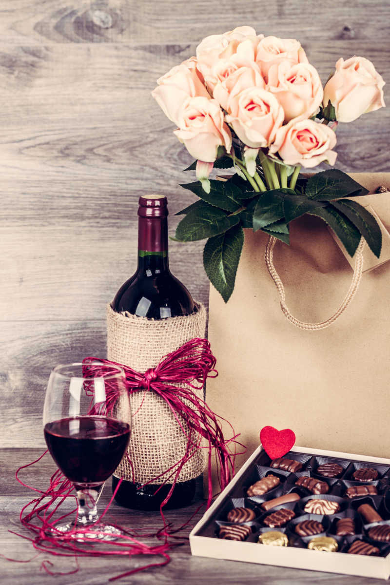 葡萄酒和巧克力盒放在红玫瑰装饰的木桌上