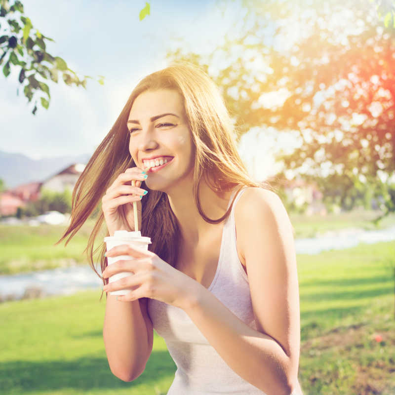 美丽快乐的年轻女子在公园喝咖啡