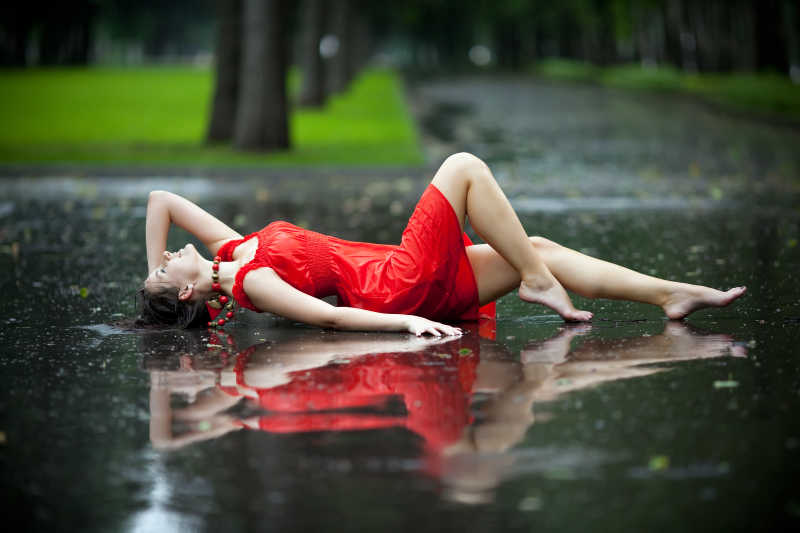 红色衣裙的女人躺在夏天的雨中