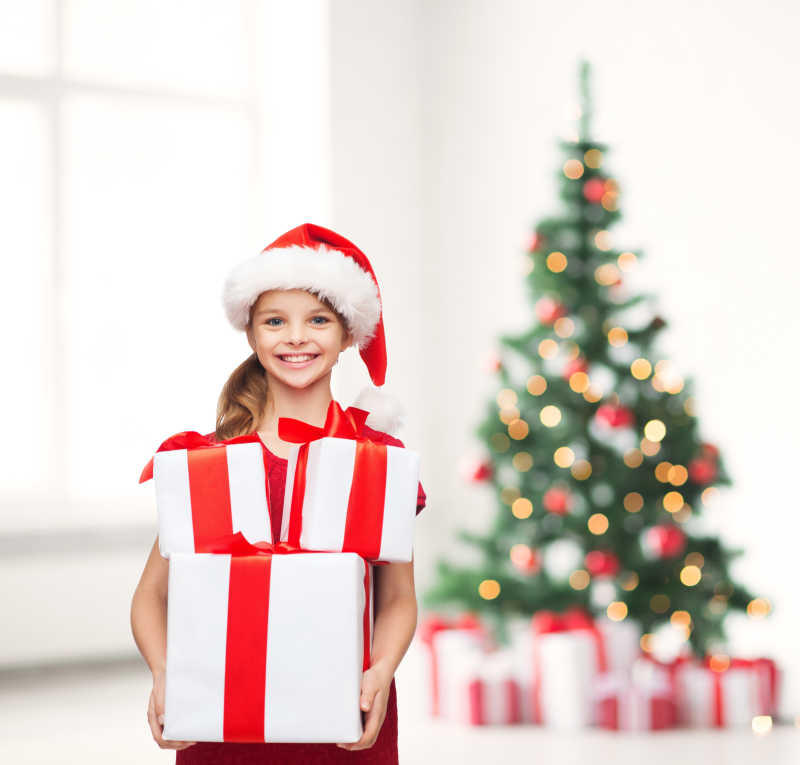 圣诞树旁抱着礼物的小女孩