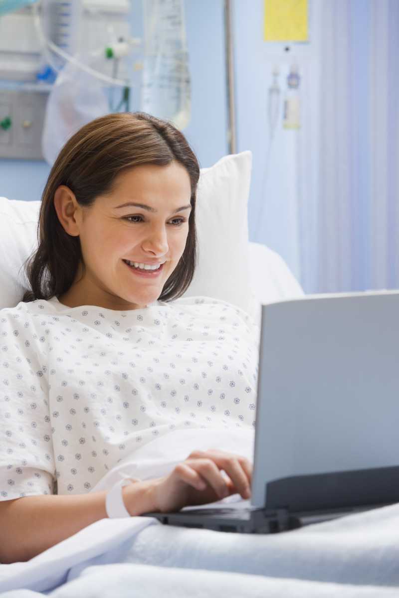 病床上看着笔记本电脑微笑的女病人