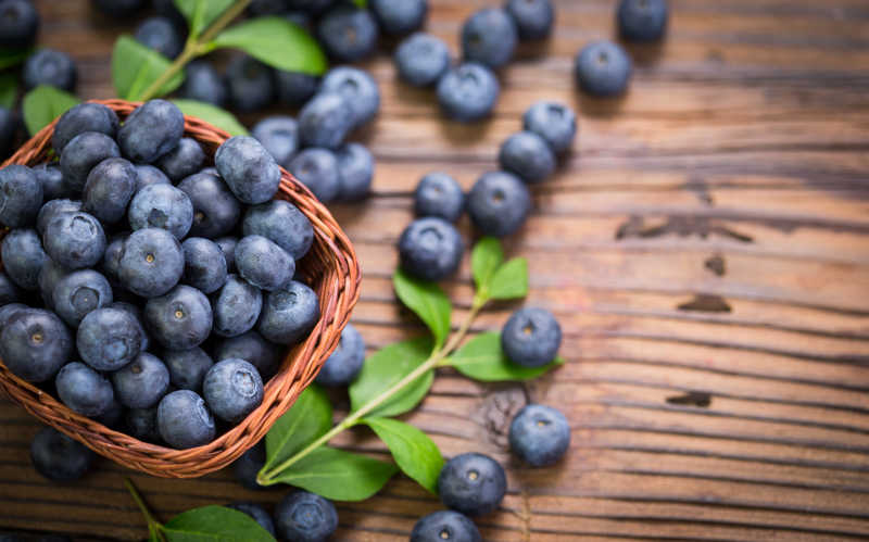 木桌上散落的蓝莓和一篮子满满的蓝莓