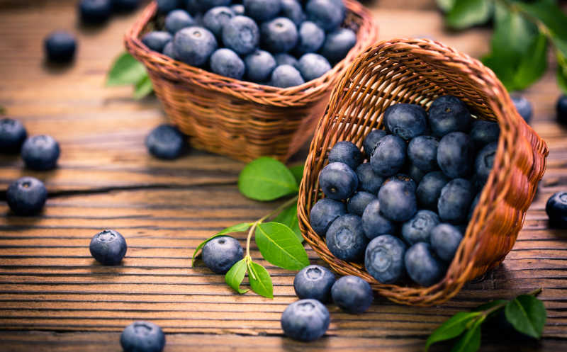 木制桌板上一览满满的蓝莓和一筐散落的新鲜的蓝莓