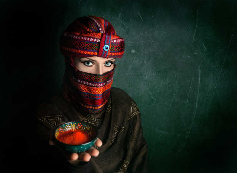绿色的纹理墙背景下戴着漂亮头巾的妇女手里端着红辣椒粉