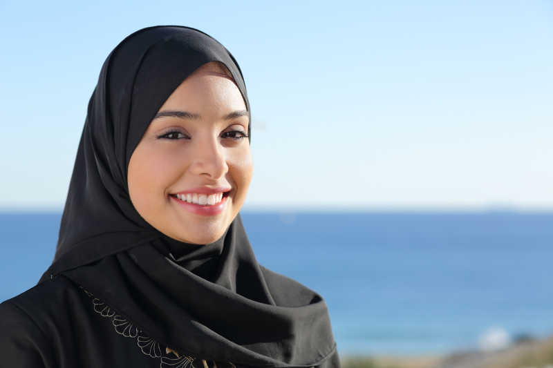 美丽的沙特女人的脸在海滩上摆着背景的大海