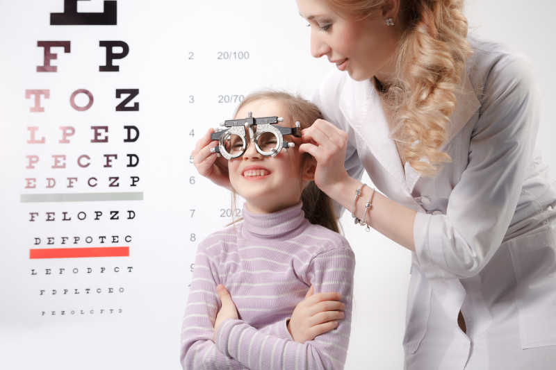 白色视力表背景下女医生使用综合验光仪给小女孩检测眼睛