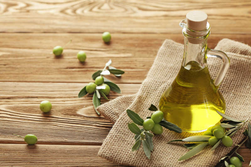 木色桌上的亚麻布上玻璃瓶子里的橄榄油和橄榄果
