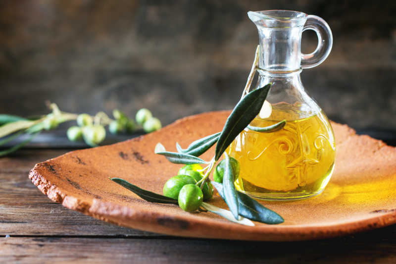 木桌上木盘里的瓶装橄榄油和新鲜橄榄果