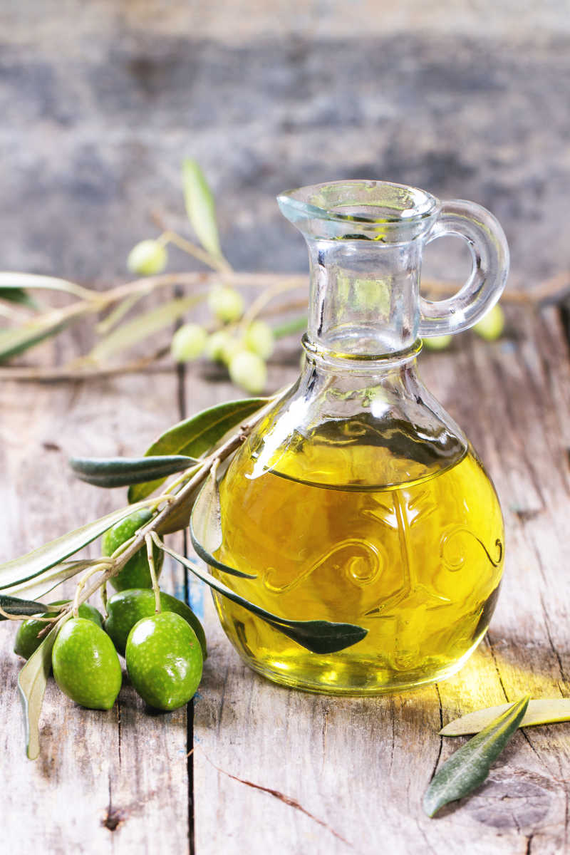 木桌上的玻璃瓶子里的橄榄油和橄榄枝