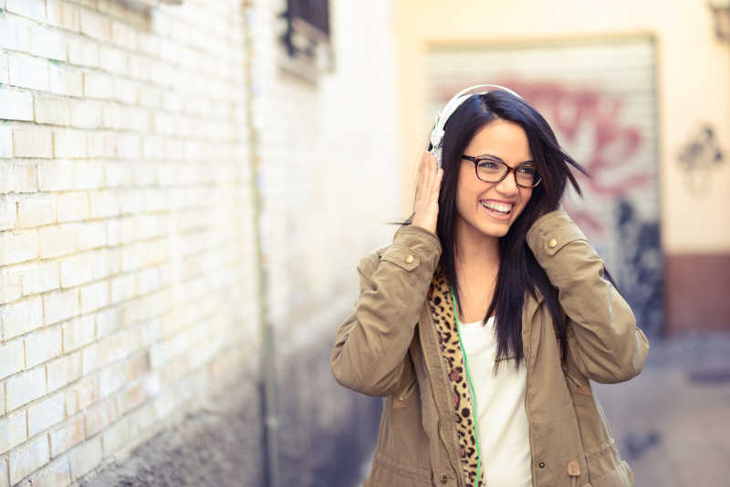 城市街道边戴着耳机听音乐的女孩