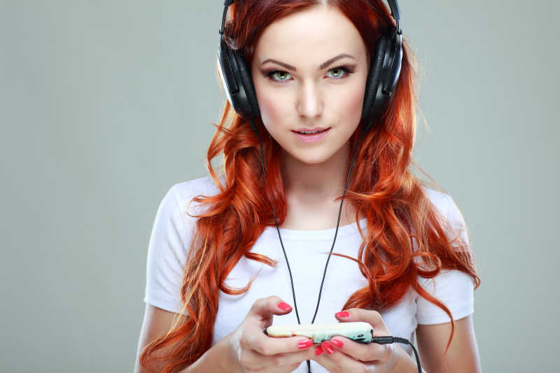 灰色背景下戴耳机的漂亮红卷发女孩