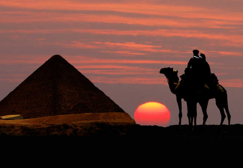 日落时分游客骑着骆驼来看金字塔