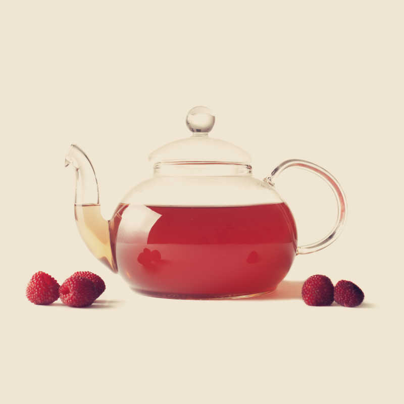 米色背景下一壶覆盆子茶和散落一旁的树莓