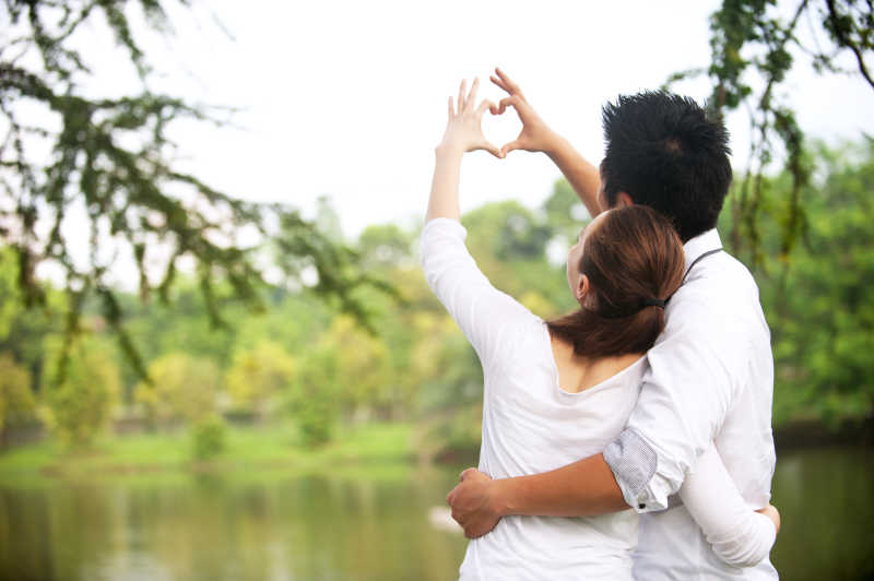 年轻夫妻对着湖面用手拼凑出心的图案