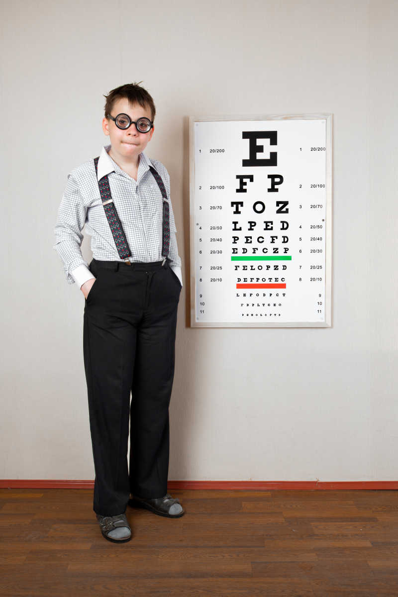 站在视力表旁边戴眼镜的男孩